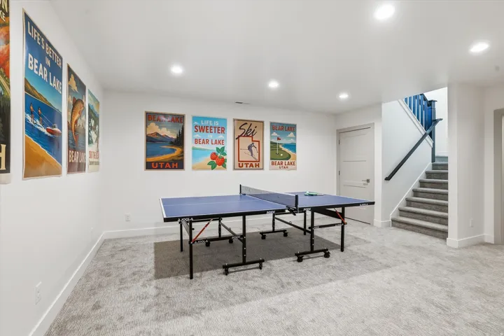 Spacious room featuring light-colored carpet, recessed lighting, a white door, and a staircase with a dark railing