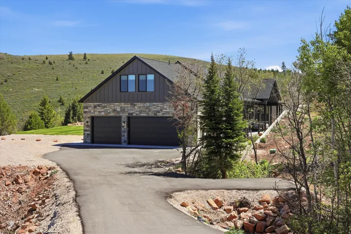 Contemporary residence featuring a two-car garage, stone and vertical siding facade, and multiple windows