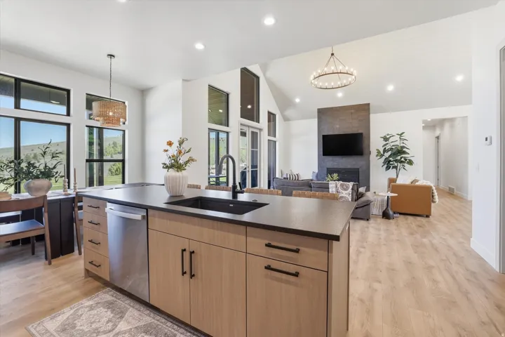 Kitchen island with a dark countertop and undermount sink, integrated stainless steel dishwasher, light wood-finish cabinetry, and black hardware