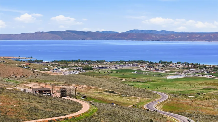 Expansive aerial landscape featuring a large body of water, distant mountain ranges, a small community along the shoreline, and verdant fields