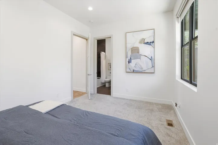 Carpeted bedroom featuring a large window with dark trim, recessed lighting, and a white baseboard