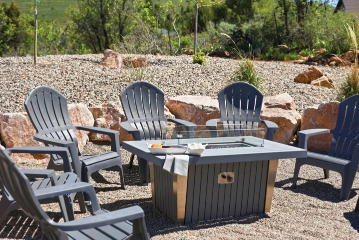 Outdoor gathering area featuring a central fire pit with a glass enclosure, surrounded by Adirondack-style chairs
