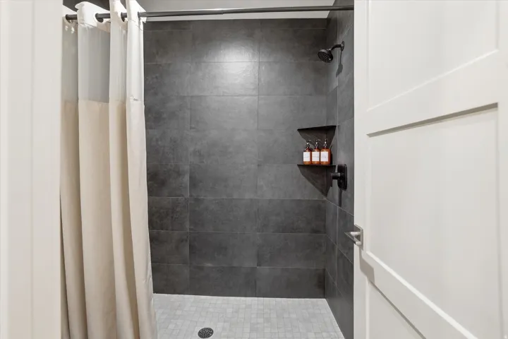 Enclosed shower featuring dark gray large-format wall tiles and a light gray mosaic tile floor