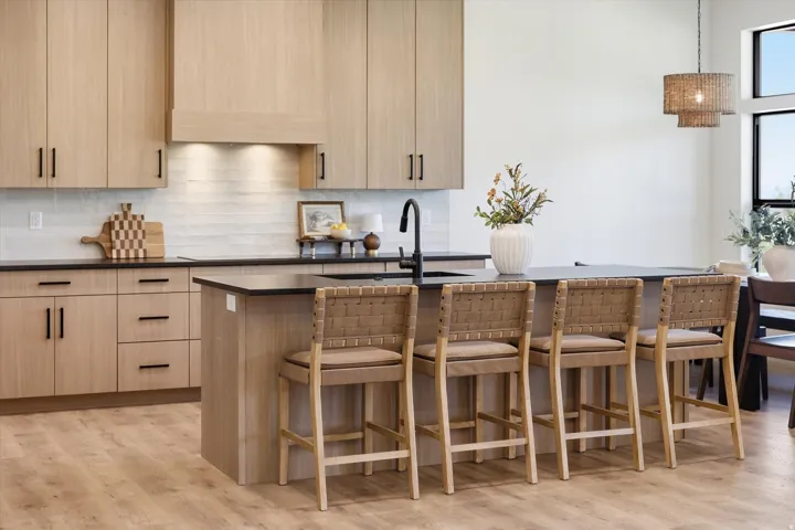 Contemporary kitchen featuring light wood-finish cabinetry, a central island with bar seating, dark countertops, and a subway tile backsplash