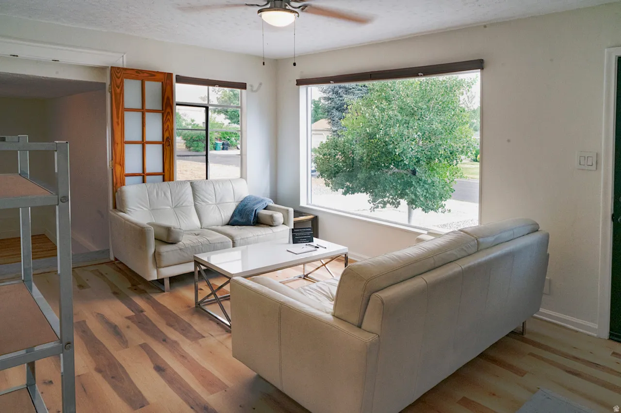 Living area with expansive windows, wood-finish flooring, a ceiling fan with integrated lighting, and a frosted pane door