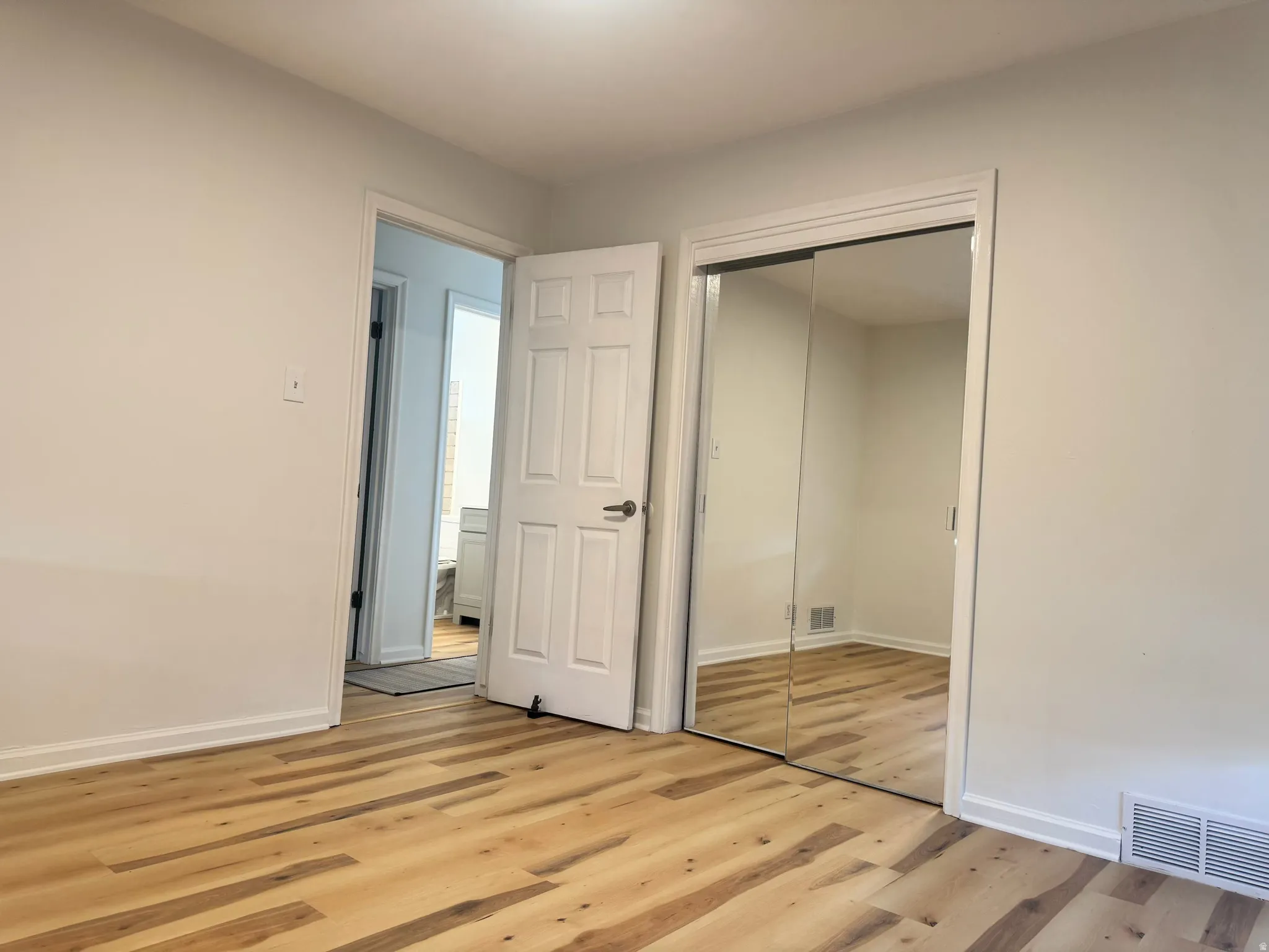 Wood-finish flooring throughout, bright white walls, and mirrored closet doors