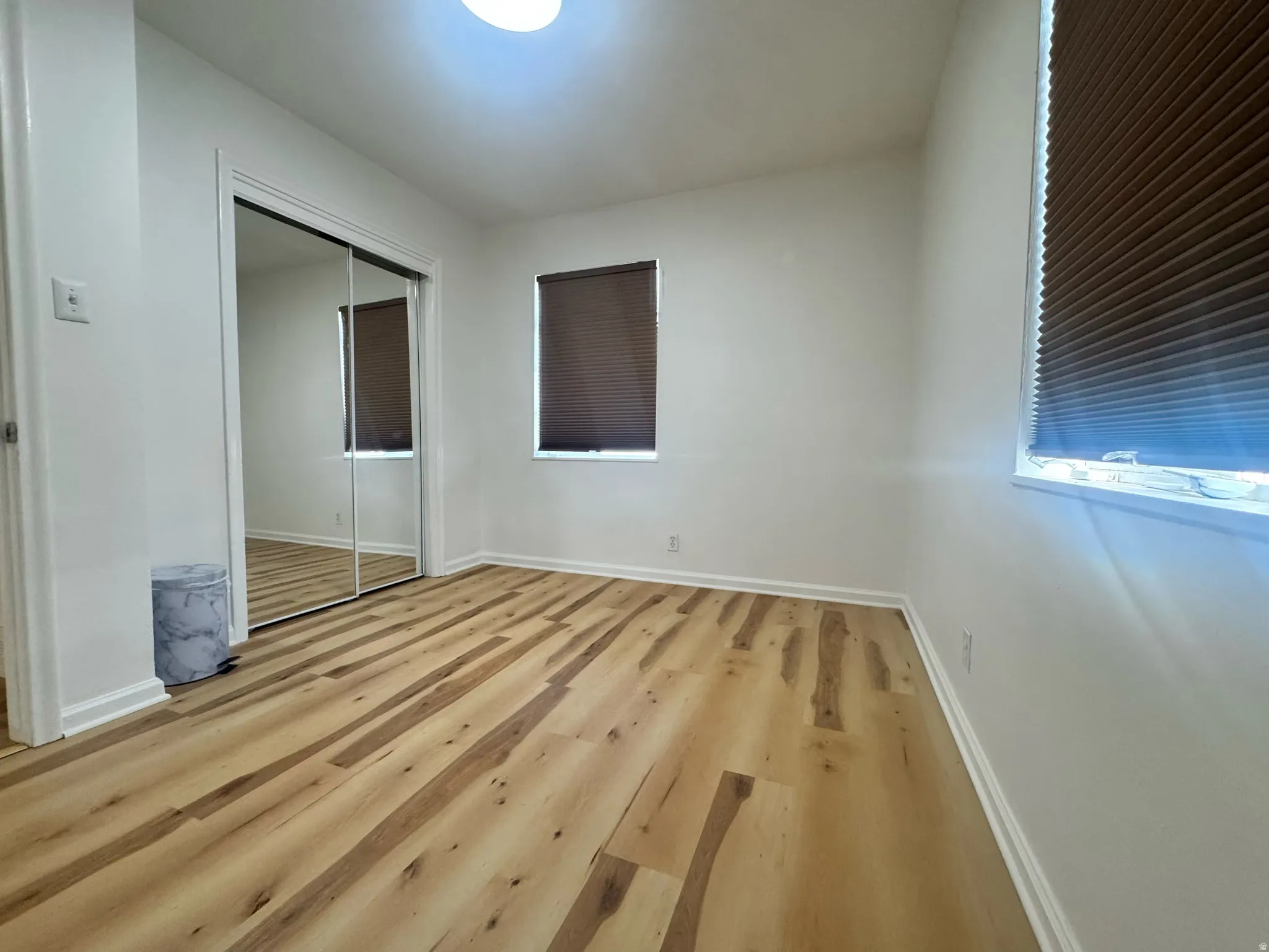 Bright interior space featuring wood-finish flooring, white walls, and two windows with brown blinds
