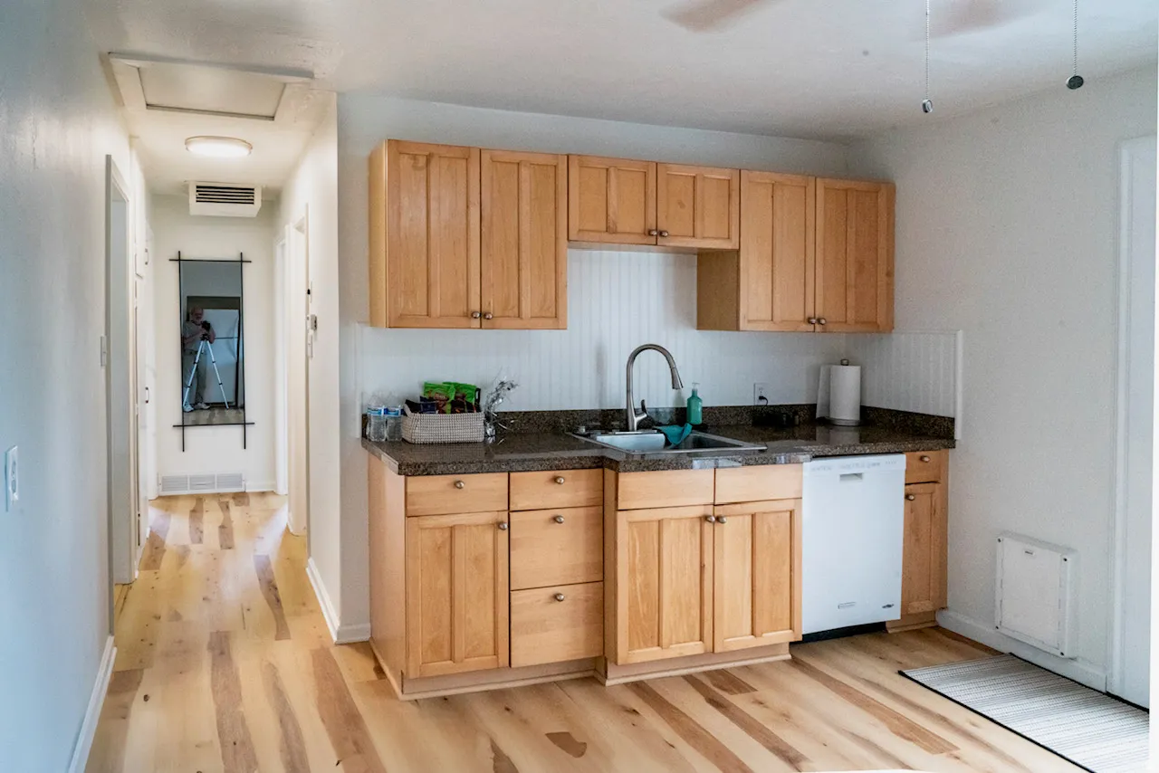 Kitchenette featuring wood-finish flooring, light wood cabinetry, granite-patterned countertops, a stainless steel sink, and white beadboard paneling