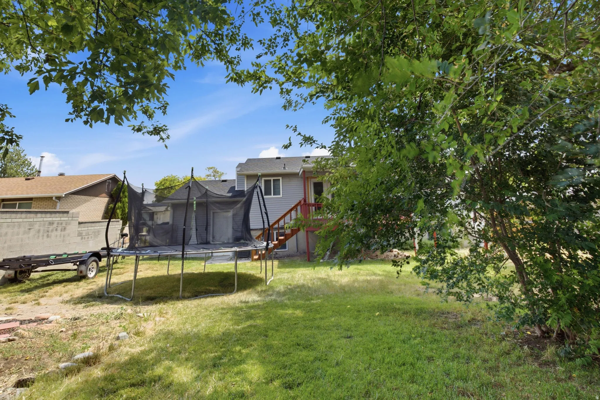 Expansive backyard featuring a green lawn, mature trees, and a concrete block retaining wall