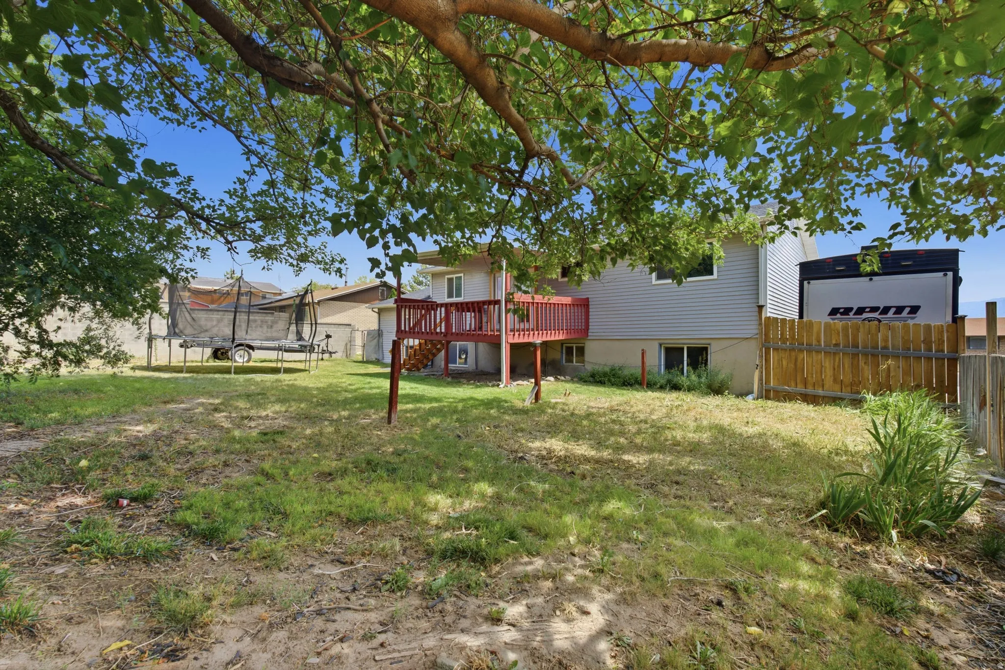 Spacious backyard featuring established trees, a two-story exterior, and a wooden deck
