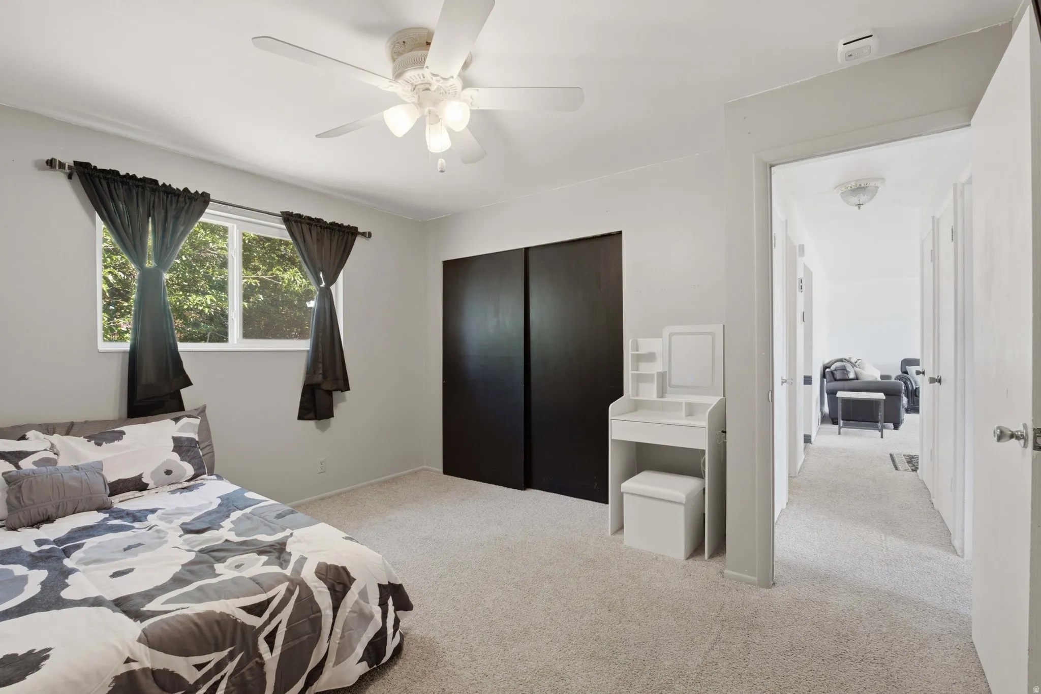 Carpeted bedroom featuring a ceiling fan with integrated lighting, a window providing natural light, and sliding dark panel closet doors