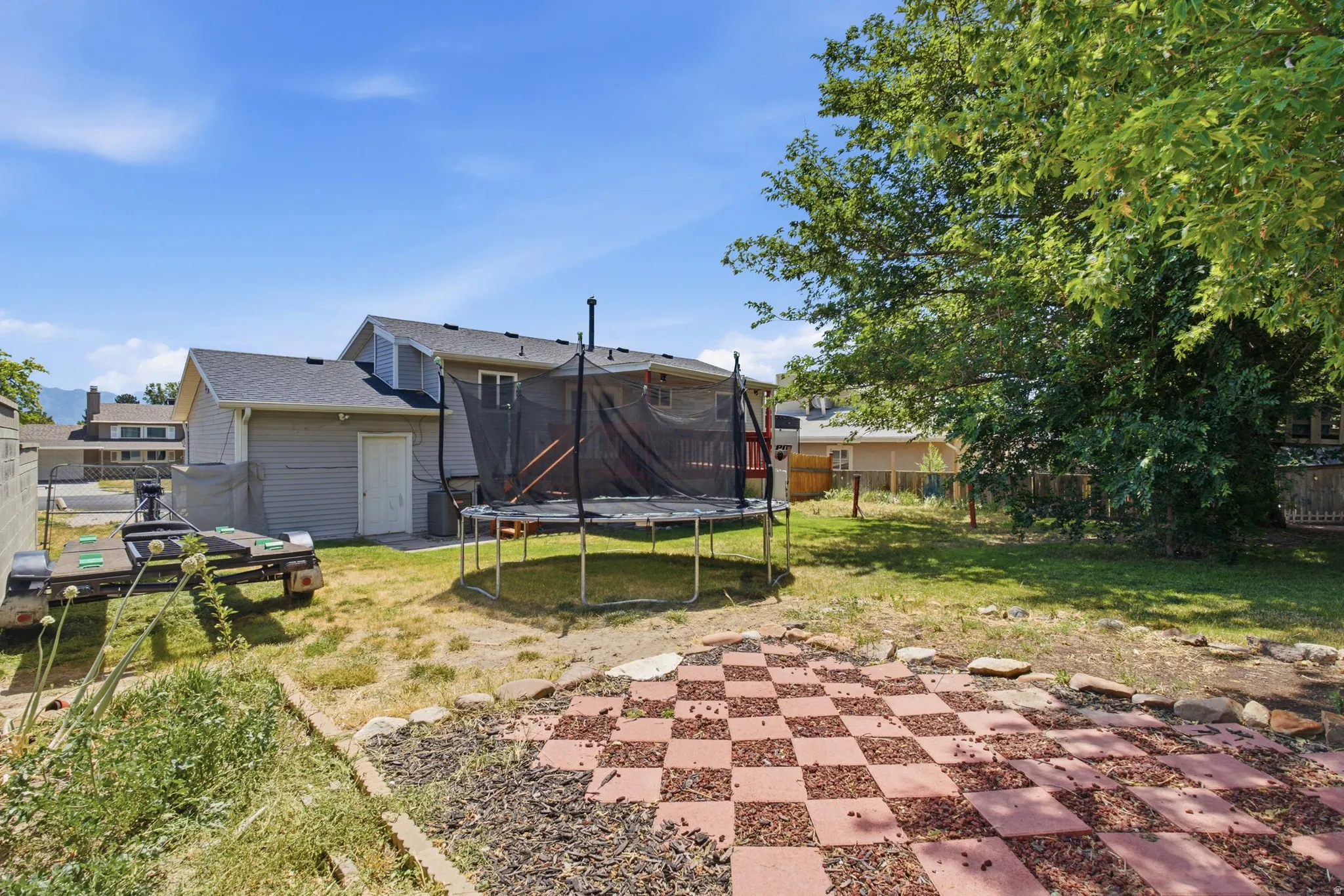 Expansive backyard featuring a checkerboard paver patio, a partial privacy fence, and mature trees