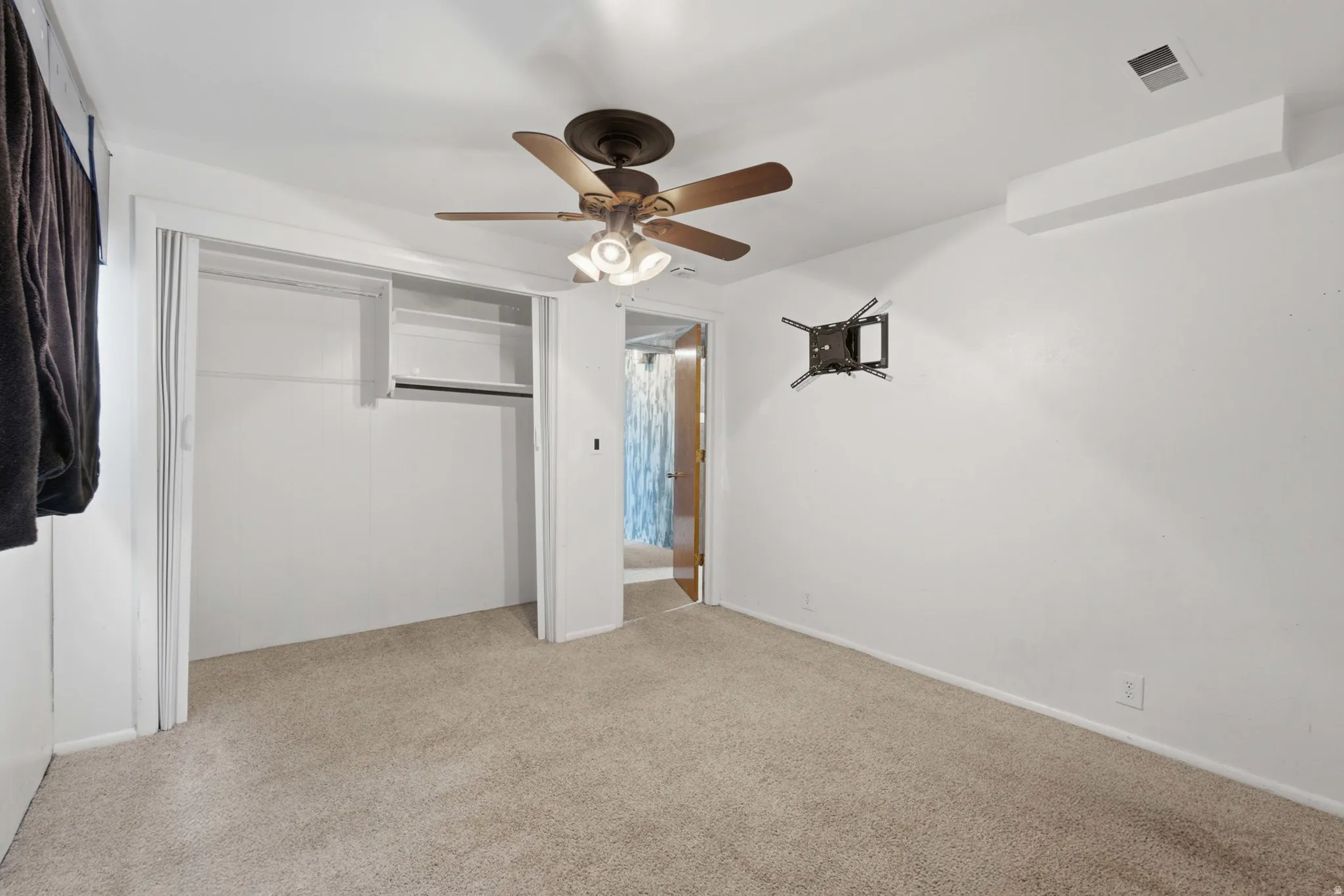 Carpeted room featuring a ceiling fan with integrated lighting, a built-in closet with shelves and hanging rod, and a wall-mounted bracket