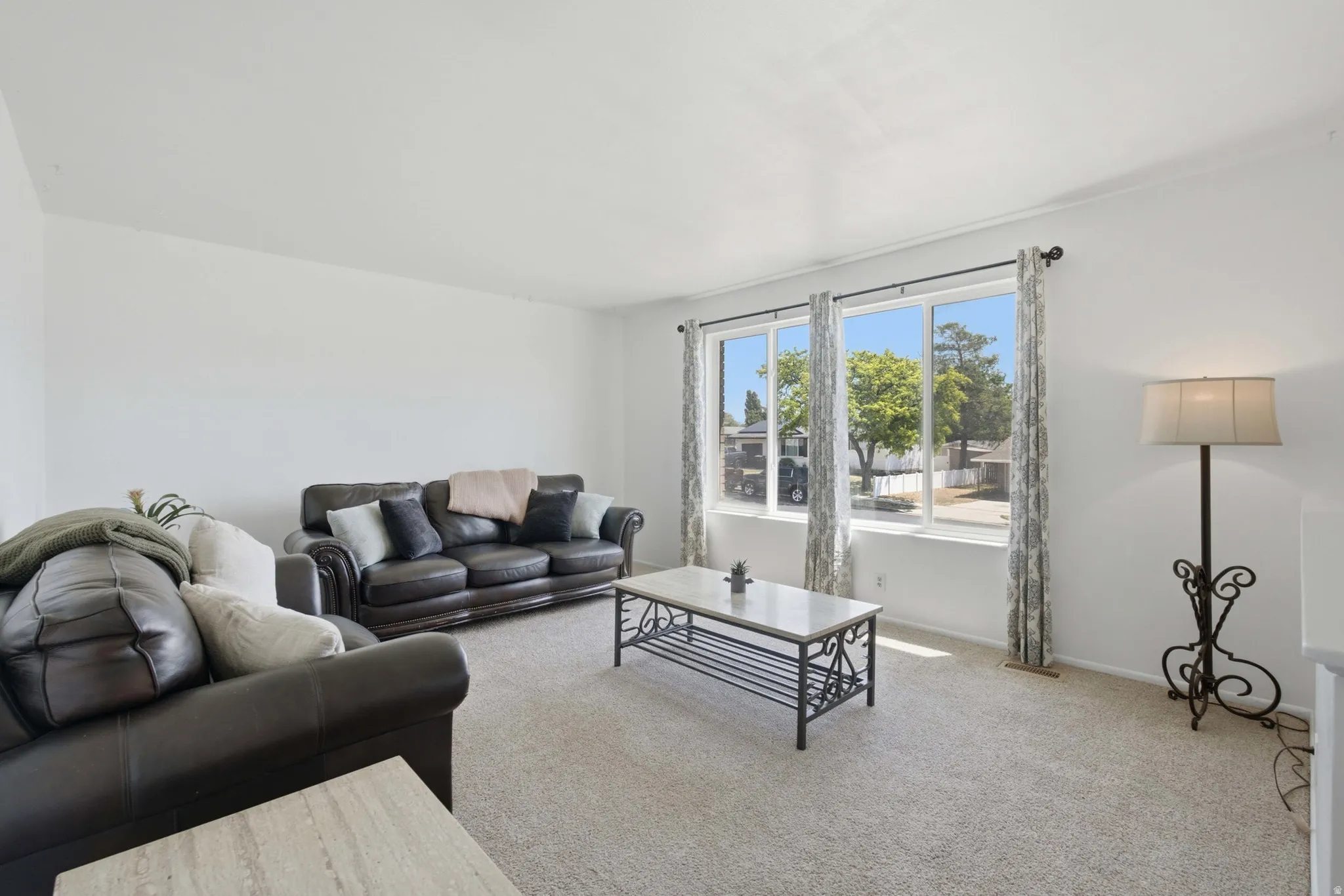 Living room featuring light-colored carpeting, white walls, and a multi-panel window with patterned drapes