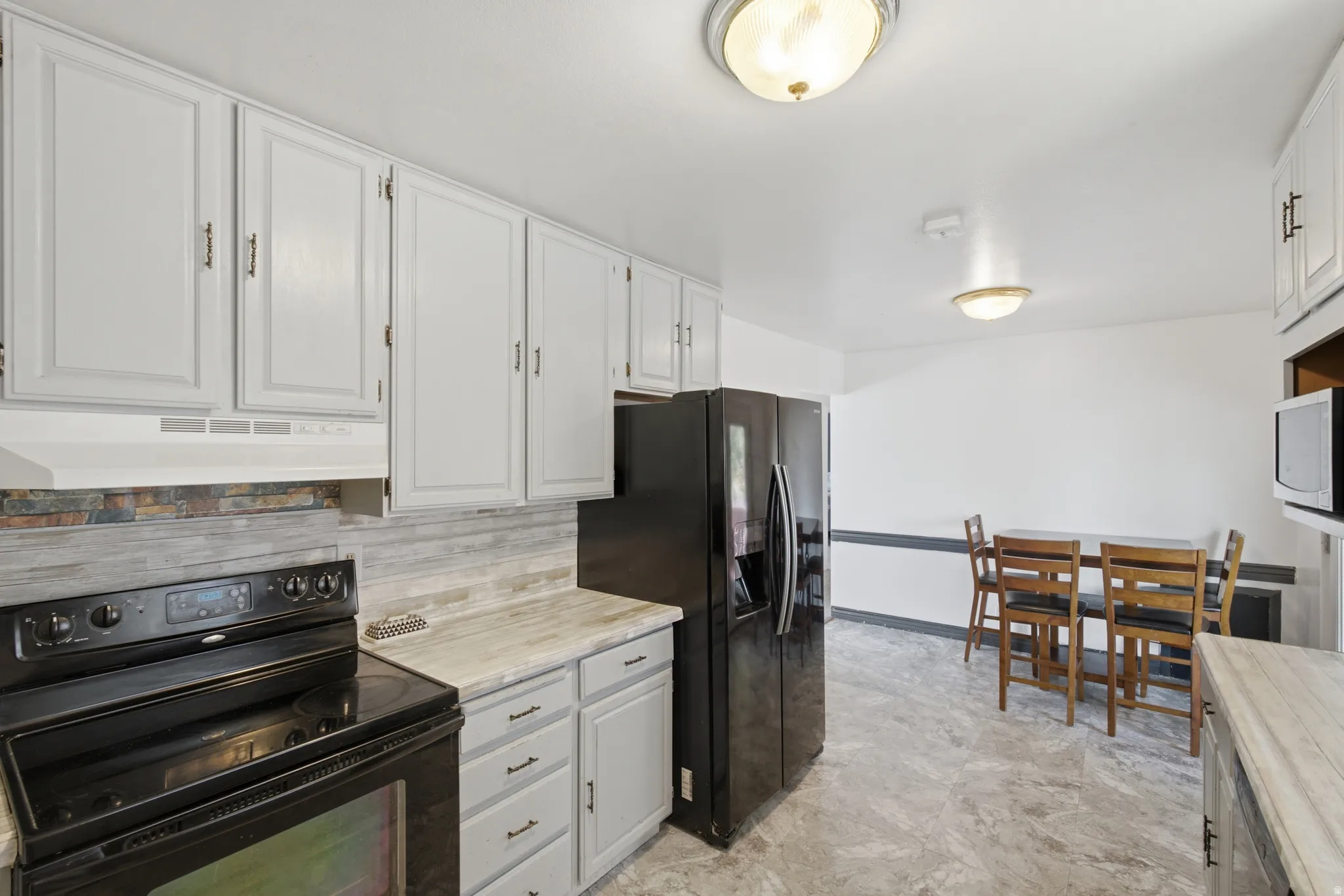 Kitchen featuring light-toned cabinetry, a black range, a dark refrigerator, and light-toned countertops