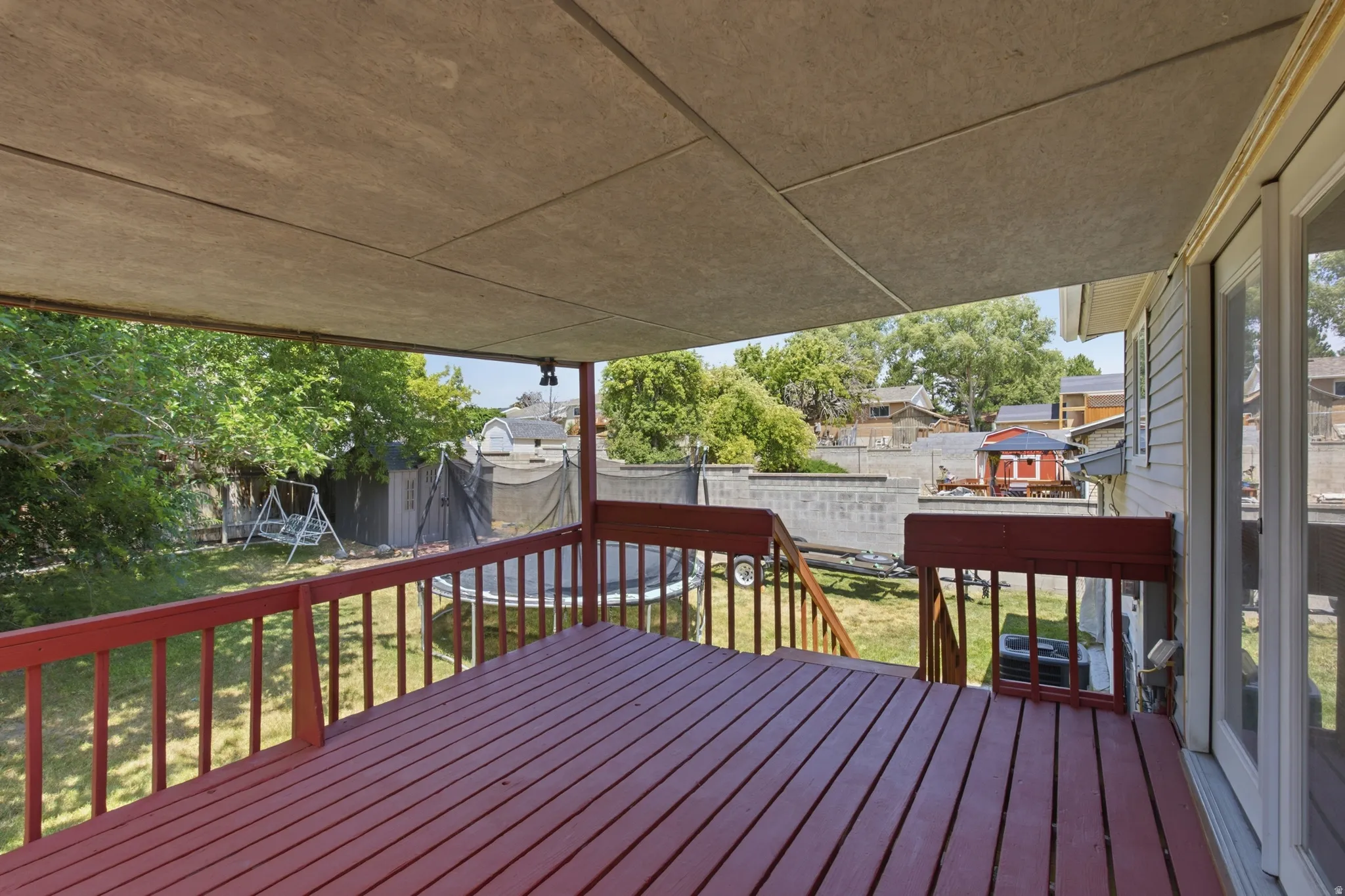 Covered deck featuring a red-stained wood-plank floor and matching railings