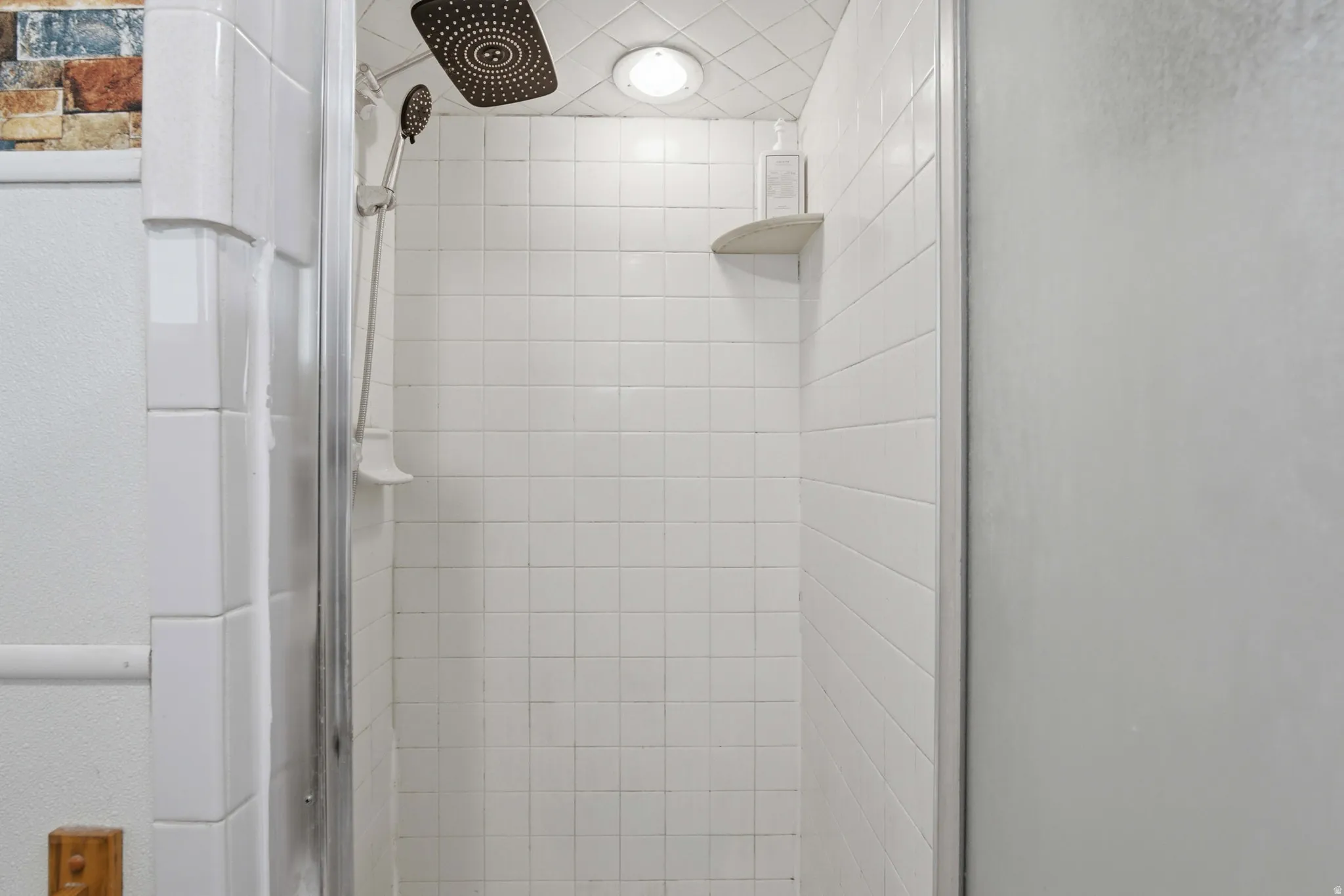 Shower enclosure featuring white square tile walls, a ceiling-mounted rainfall showerhead, and an adjustable handheld shower spray
