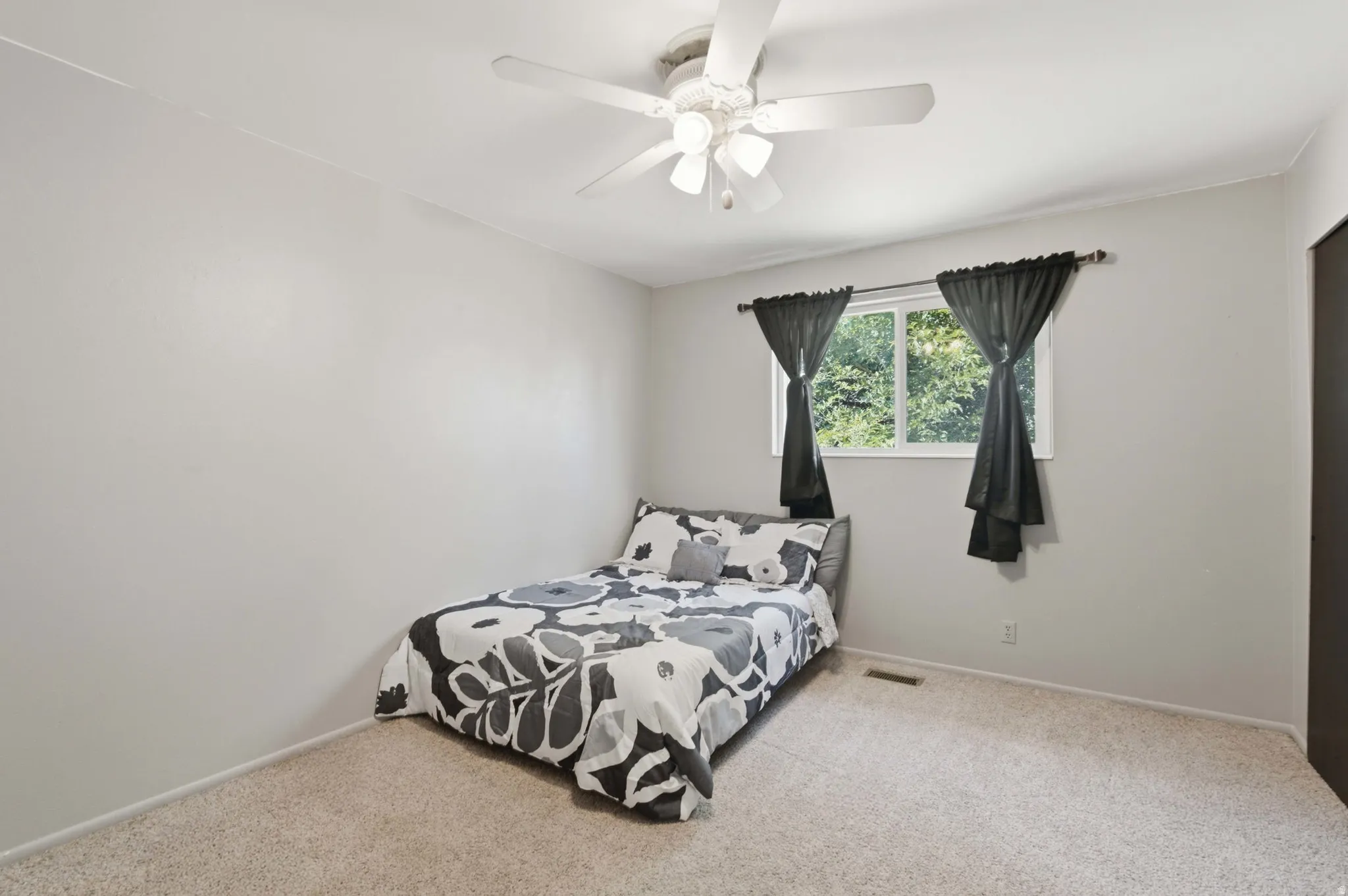 Carpeted interior room featuring light-toned walls, a white ceiling fan with integrated lighting, and a double-pane window