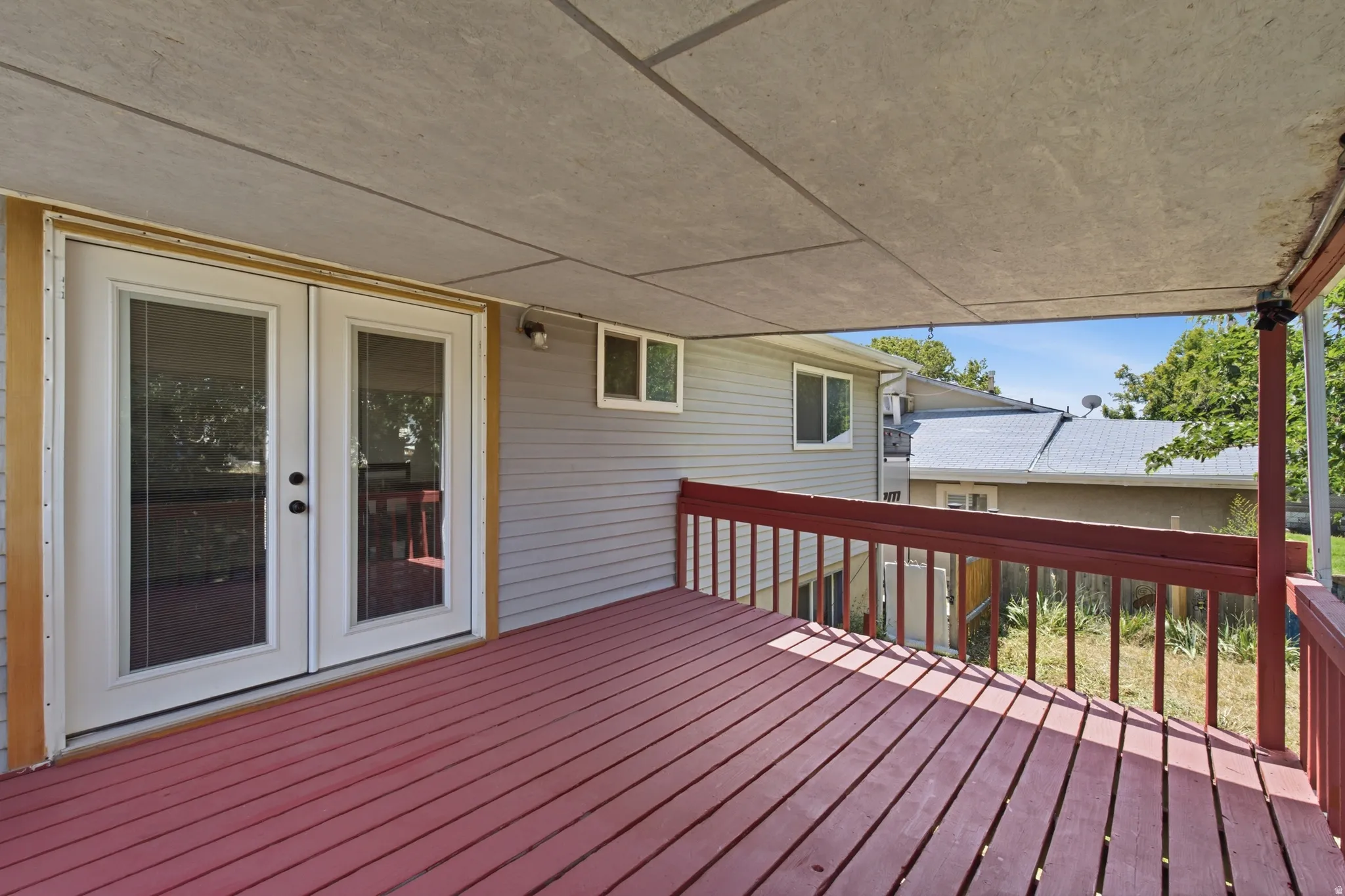 Covered wooden deck featuring a red-stained surface, painted railings, and a pair of white-framed glass French doors