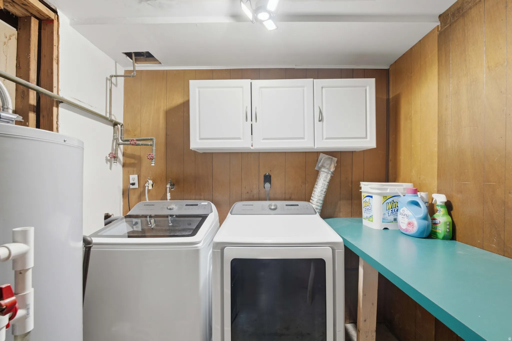 Dedicated laundry area featuring a water heater, washer, dryer, built-in cabinetry, and a countertop workspace