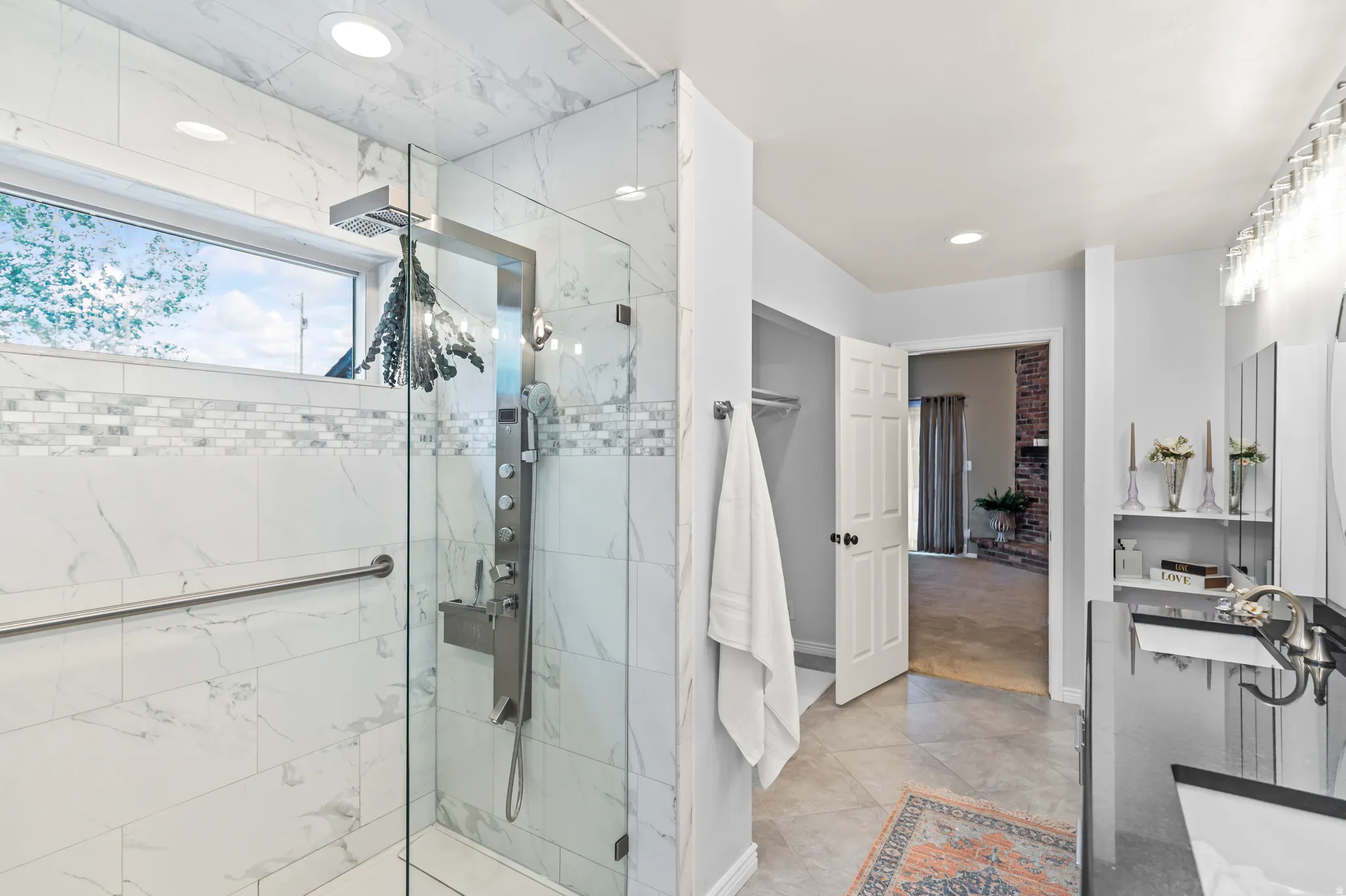Walk-in shower featuring large format wall tile with a mosaic accent band, a multi-function shower panel, and a clear glass enclosure