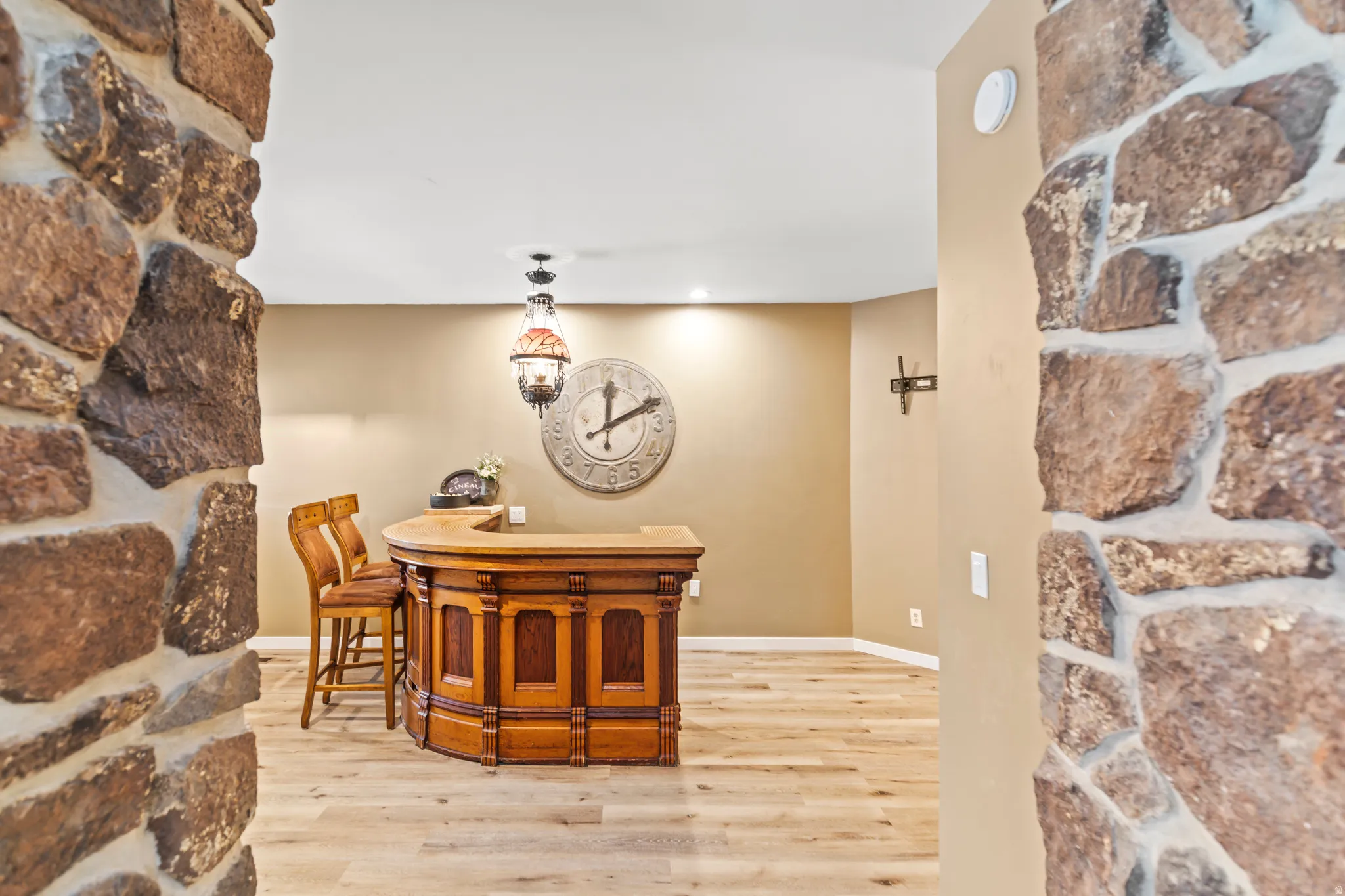 Built-in wood bar with a stone counter, light wood-finish flooring, recessed lighting, and stone columns
