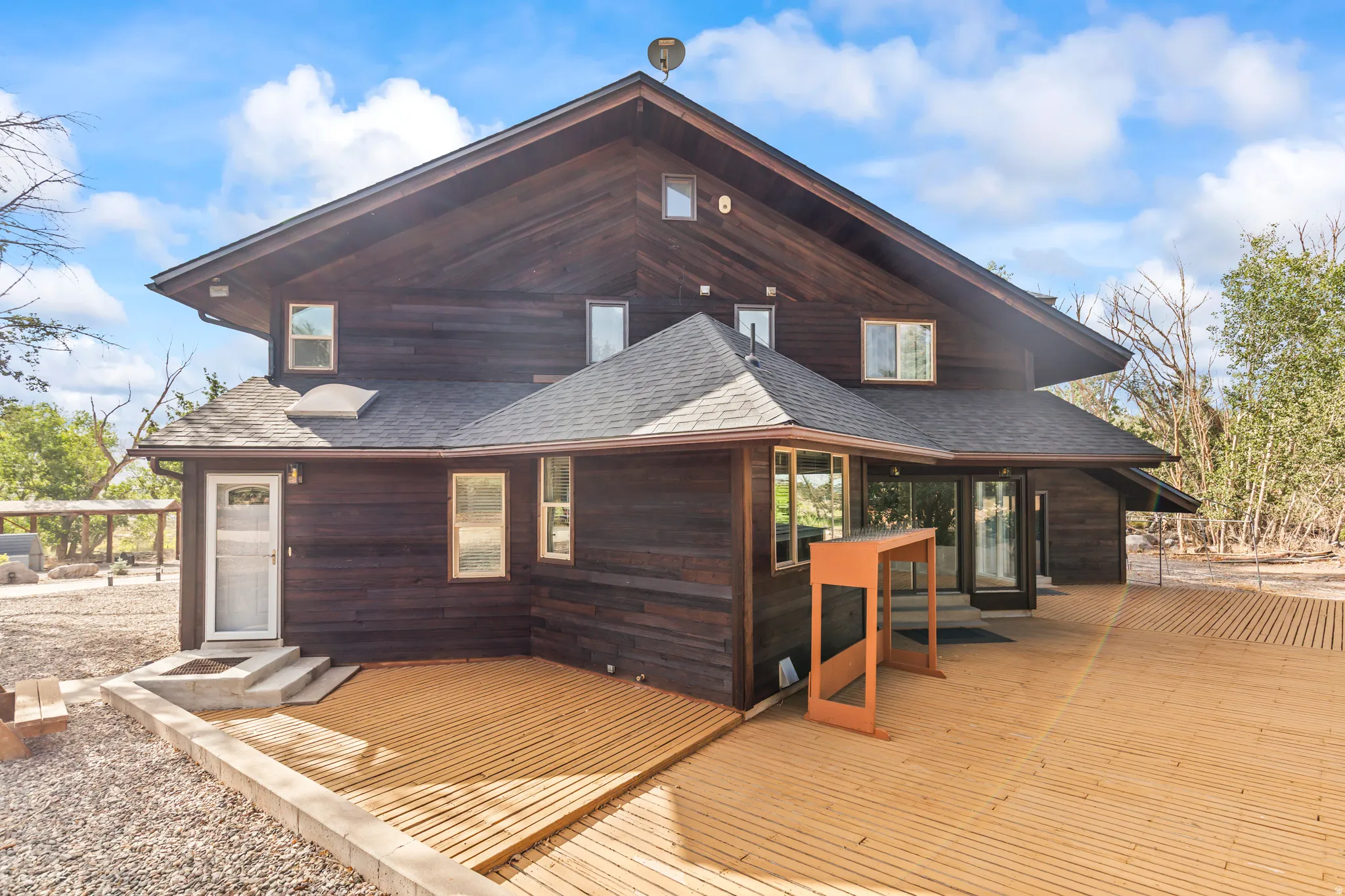 Multi-level dark-stained wood exterior featuring a spacious wood deck, multiple windows, and a dark shingled roof