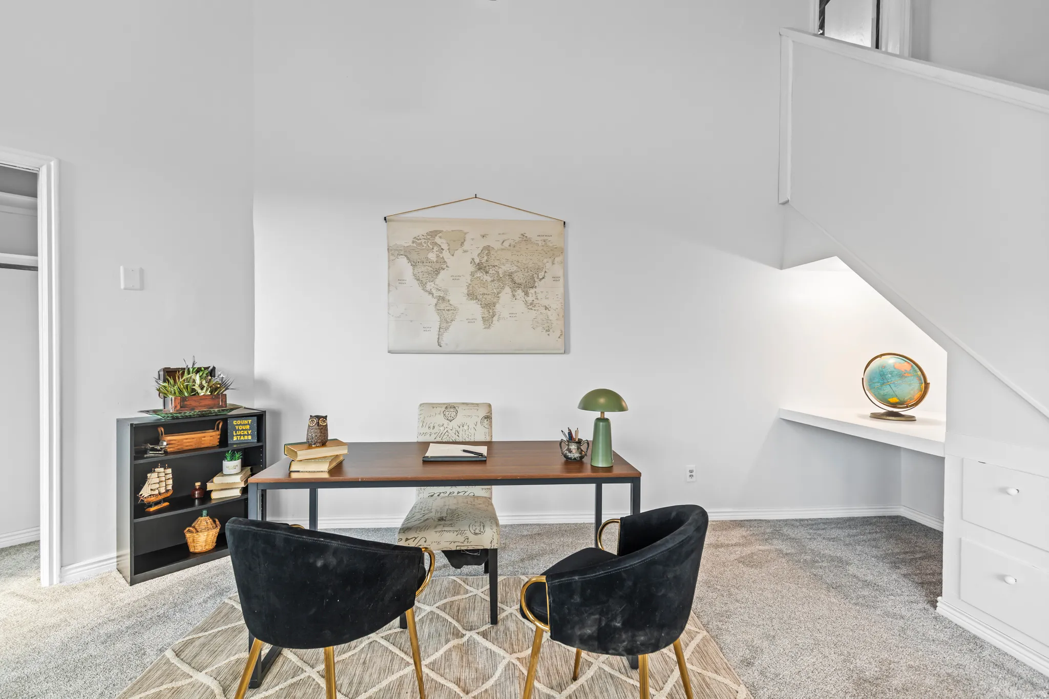 Carpeted area featuring built-in shelving, white walls, and a built-in desk under the staircase