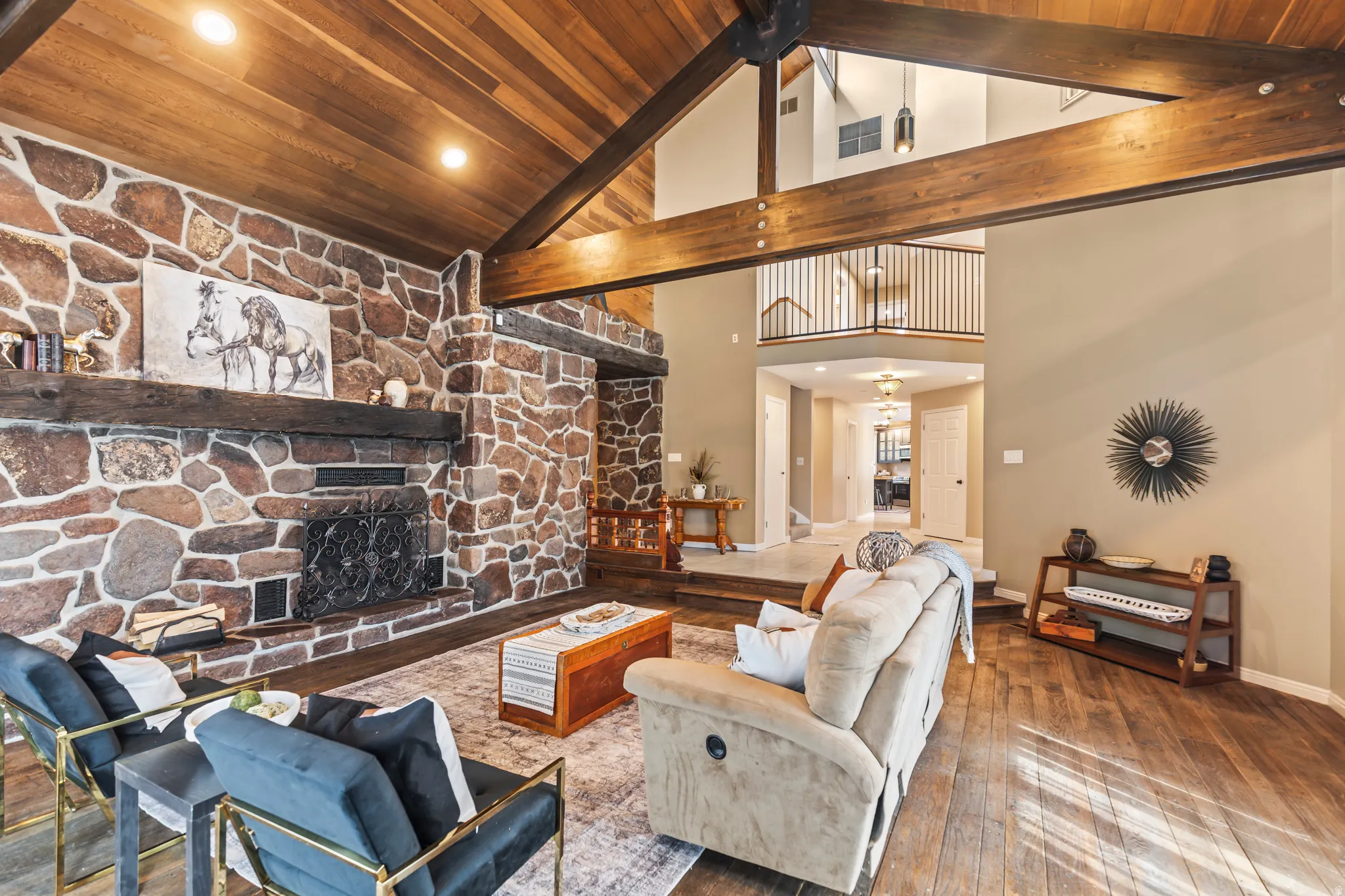 Spacious living area featuring a vaulted wood-paneled ceiling with exposed beams, a stone fireplace with a substantial wood mantel, recessed lighting, and wood-finish flooring