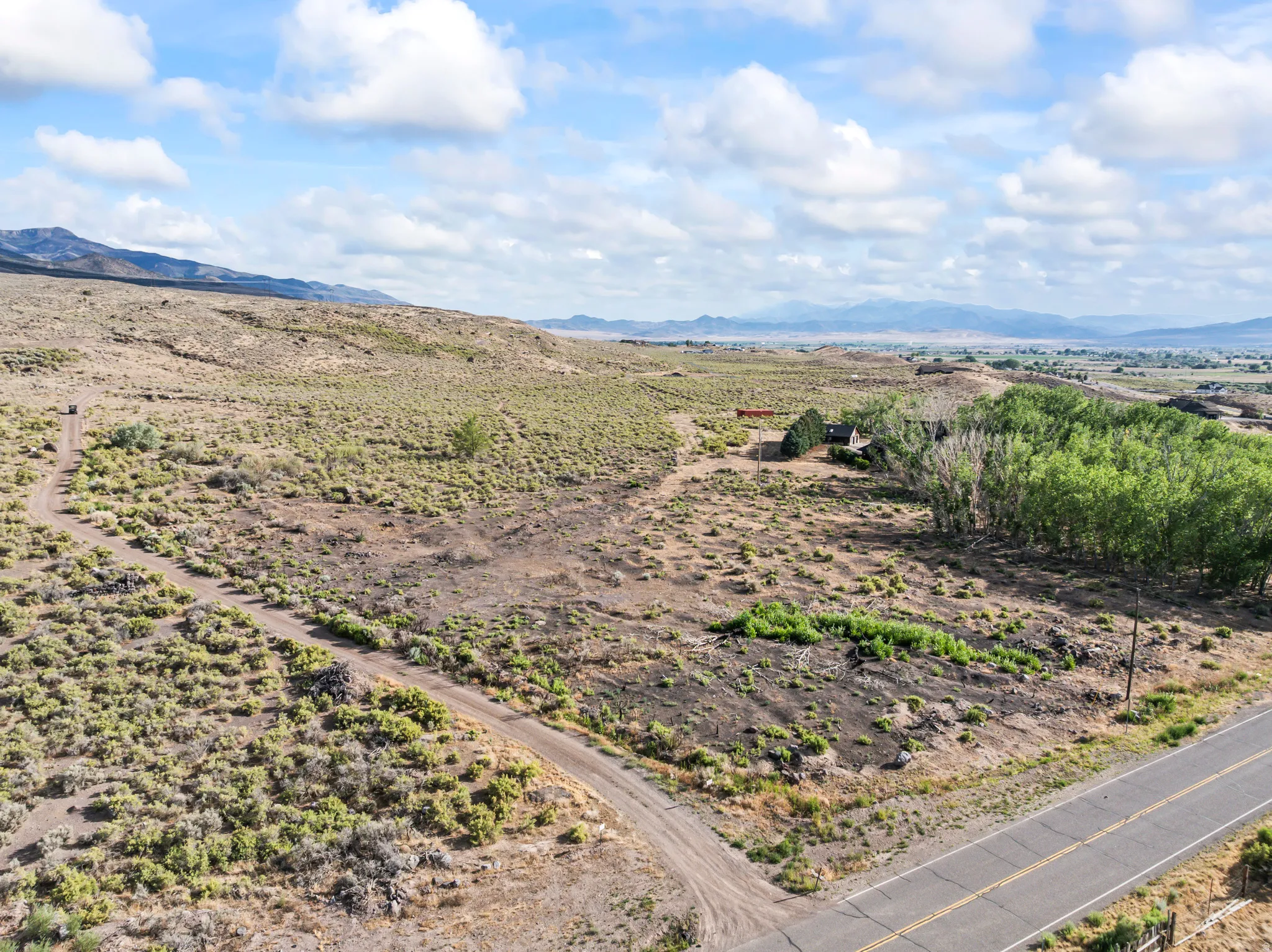Expansive undeveloped land featuring natural vegetation, a paved road border, and a distant mountain range backdrop