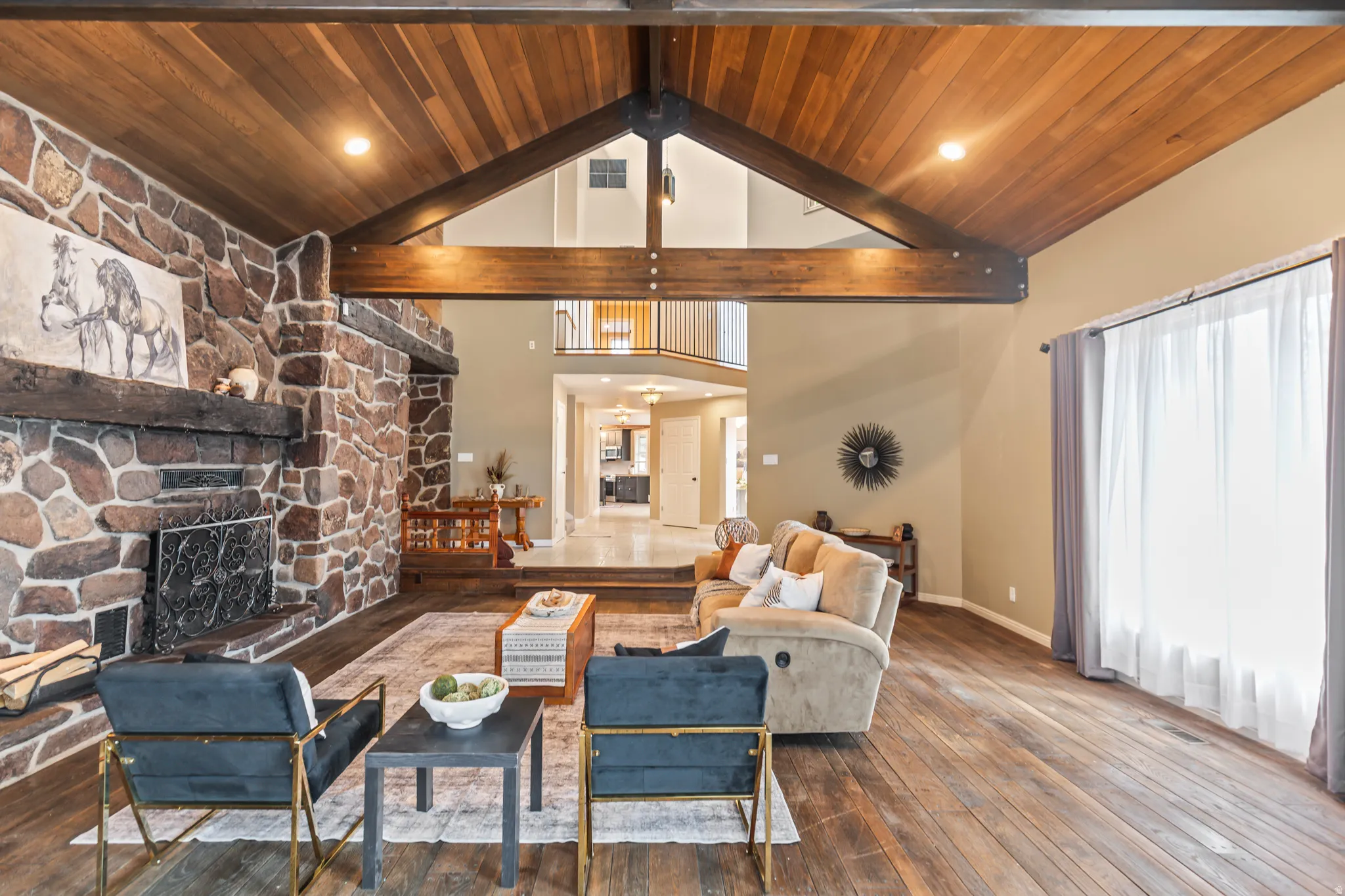 Great room featuring a vaulted wood-paneled ceiling with exposed beams, a floor-to-ceiling natural stone fireplace, and wood-finish flooring