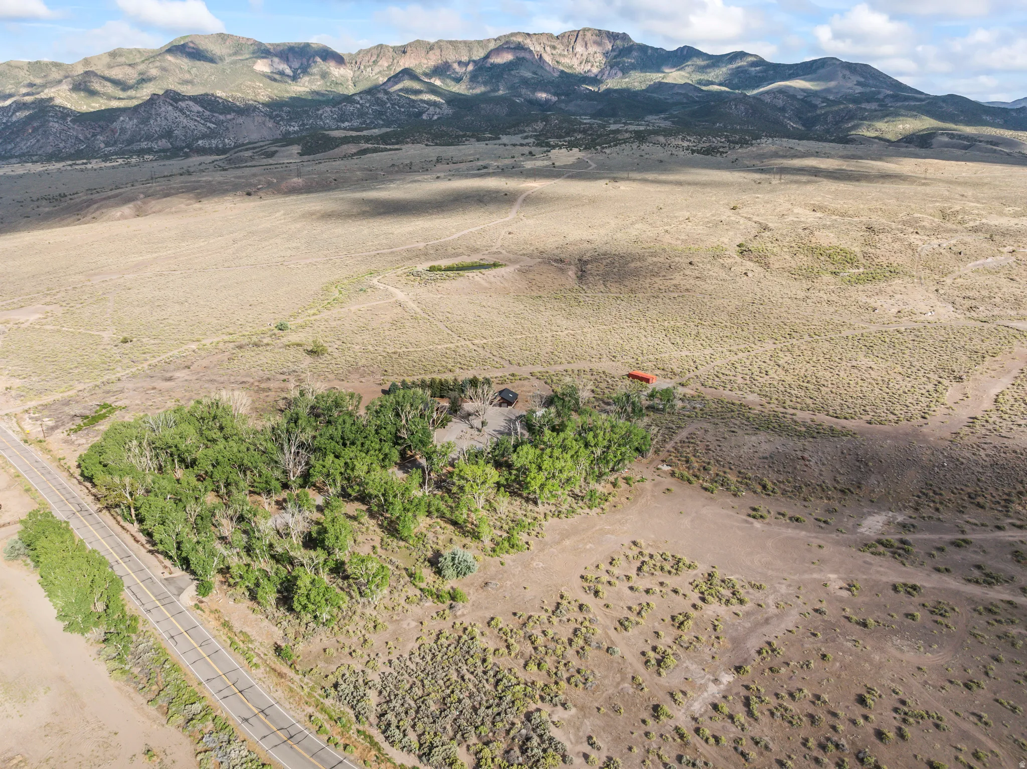 Expansive rural property featuring a paved road frontage, mature trees, open land, and mountain backdrop