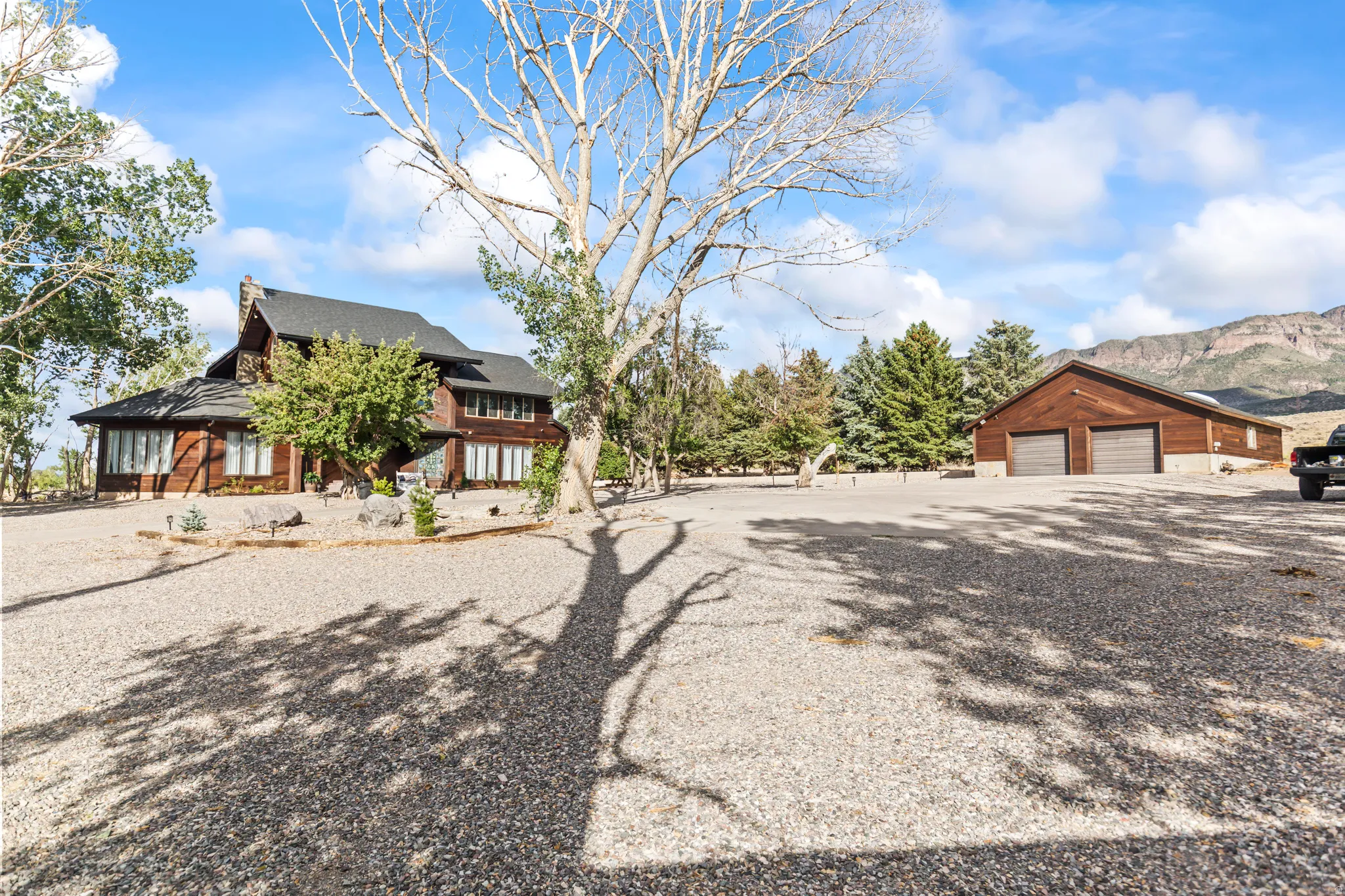 Expansive gravel driveway providing extensive parking, complemented by a two-story residence featuring wood siding and a prominent chimney structure