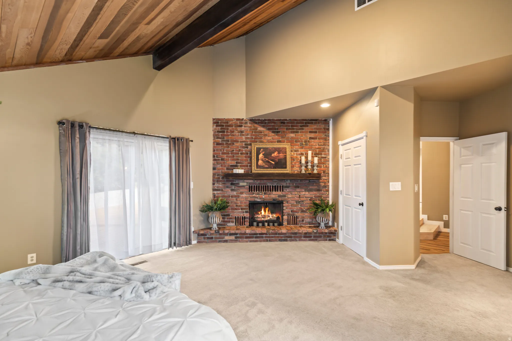Corner brick fireplace with a wood mantel, vaulted wood-plank ceiling with exposed beams, light-colored carpet, and sliding glass door