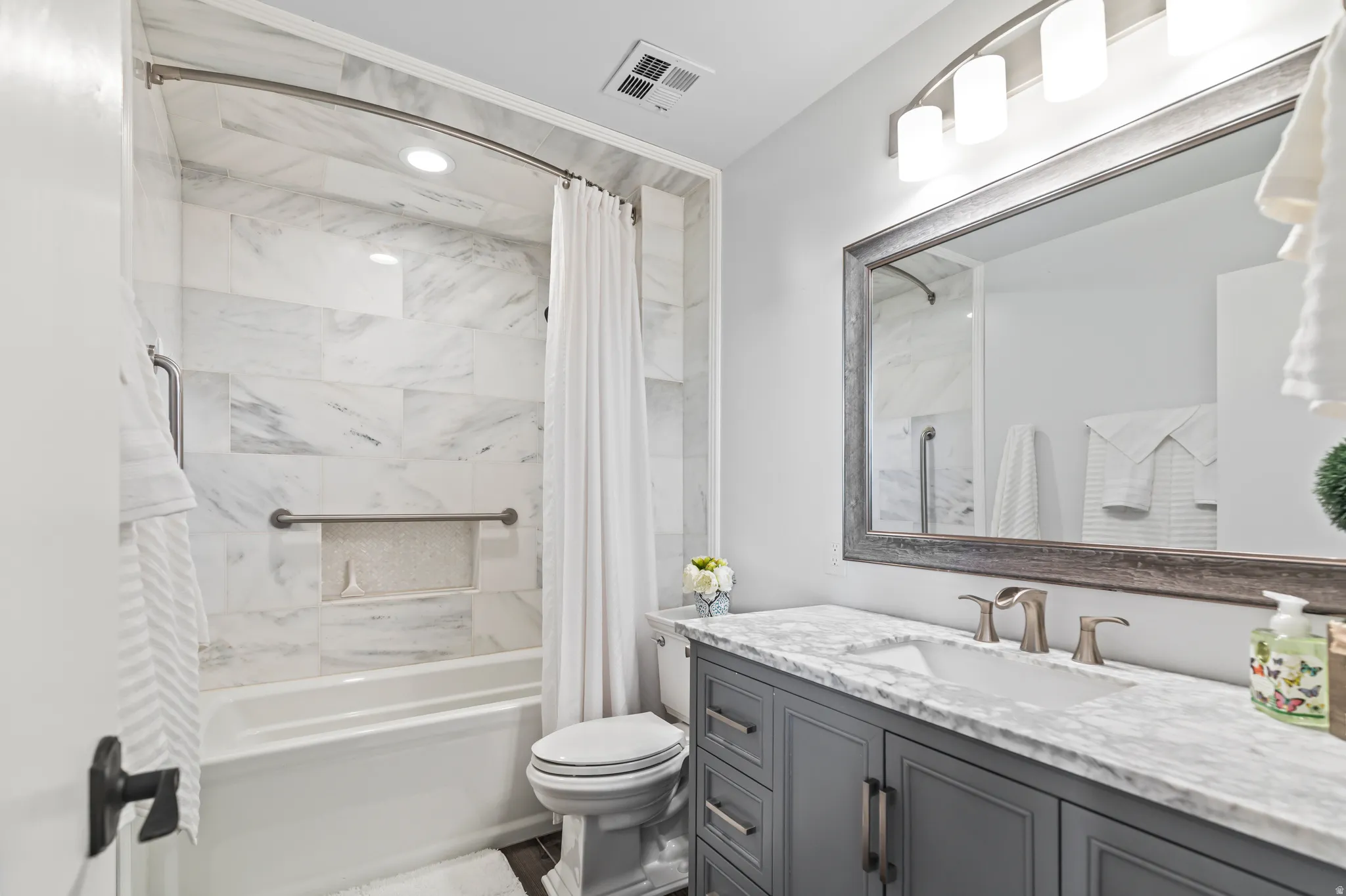 Bathroom featuring a white bathtub with marble-look tile surround, a built-in shower niche, and a curved shower rod