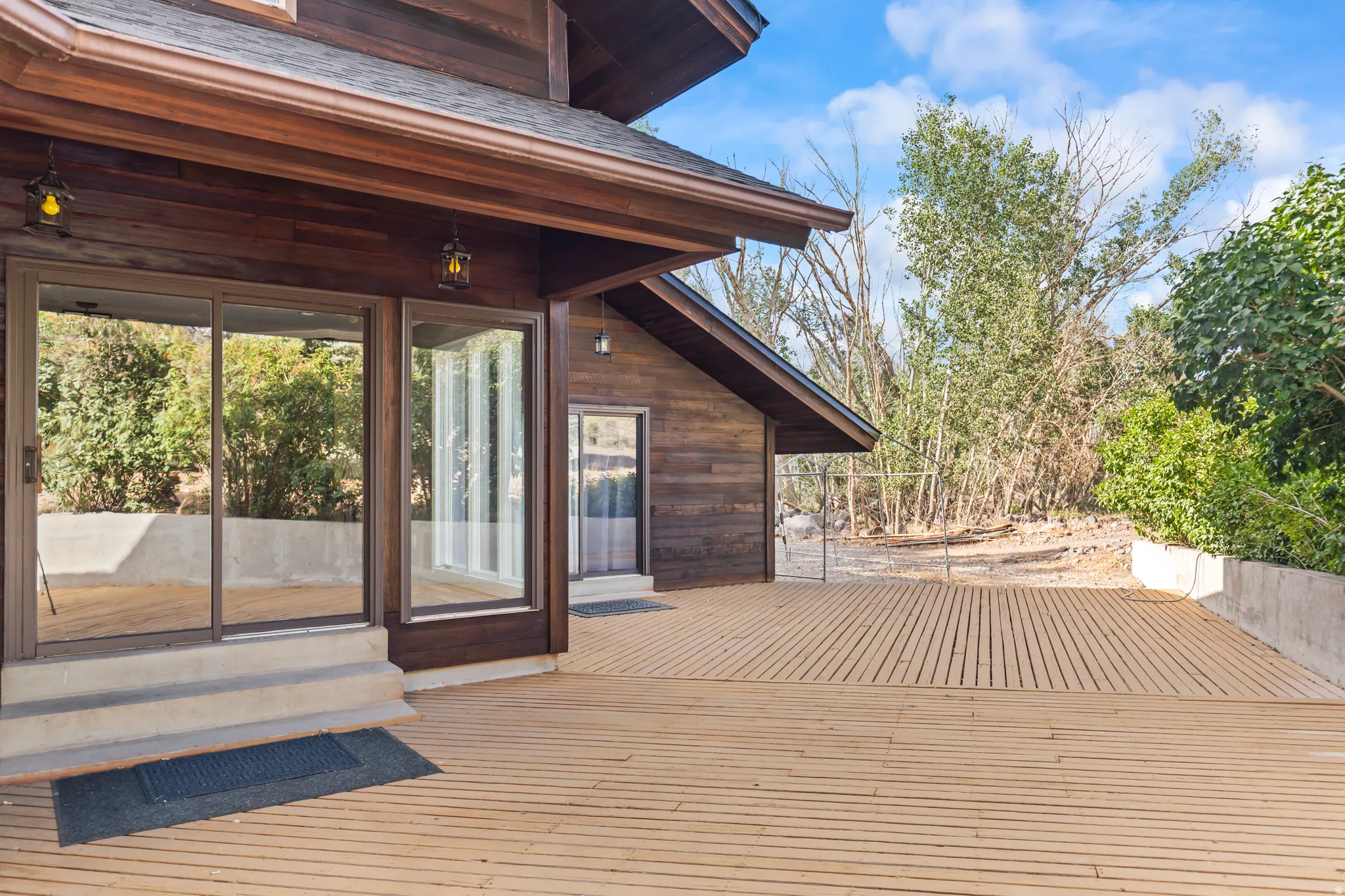 Expansive outdoor decking crafted from light wood, featuring a concrete retaining wall and mature surrounding foliage