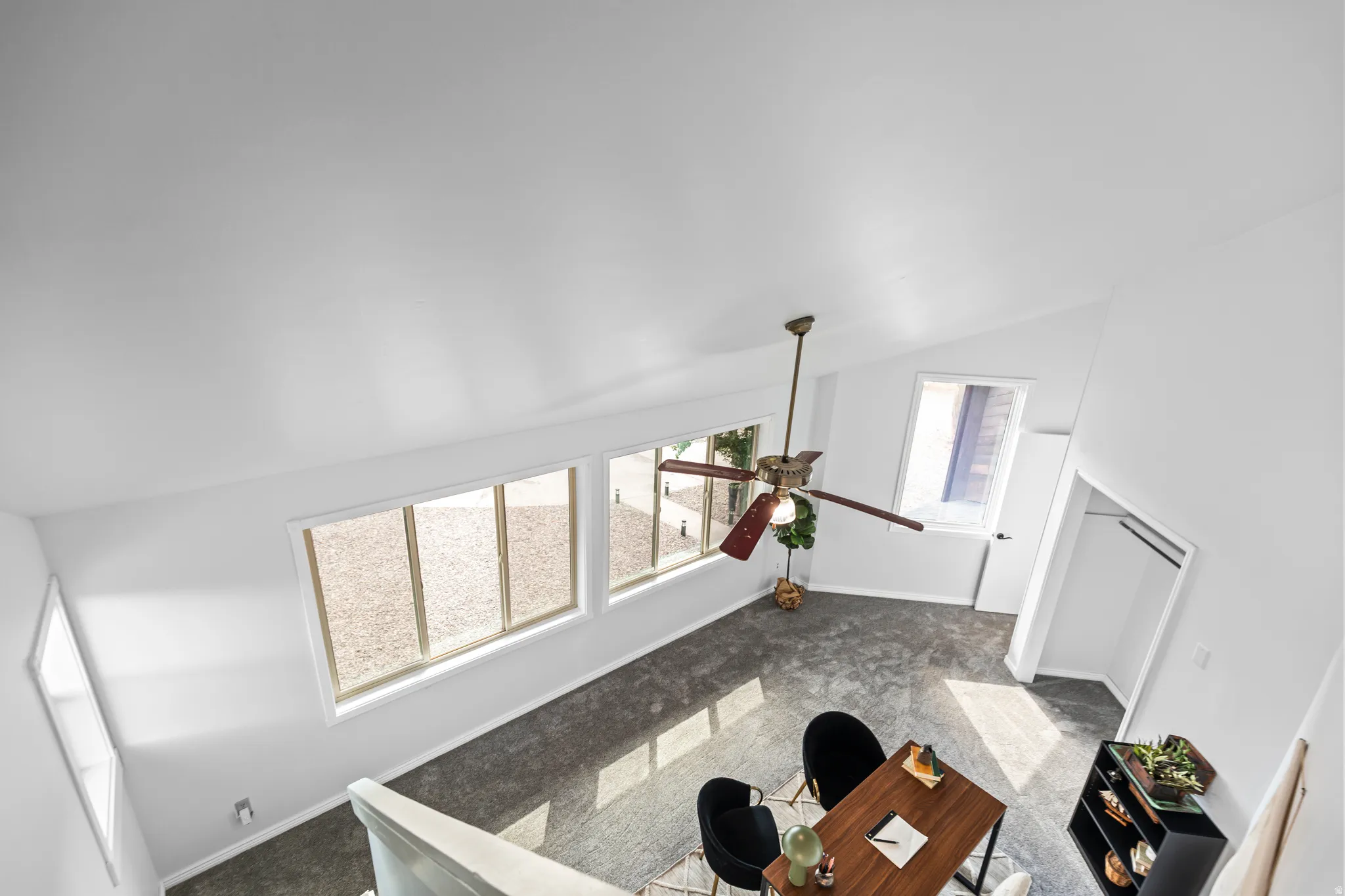 Vaulted white ceiling with a ceiling fan, multiple windows with white trim, and a built-in closet with hanging rods