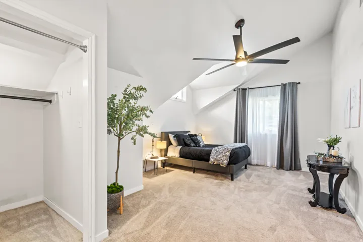 Carpeted bedroom featuring a vaulted ceiling with a ceiling fan, a window with curtains, and a built-in closet with shelving and hanging rod