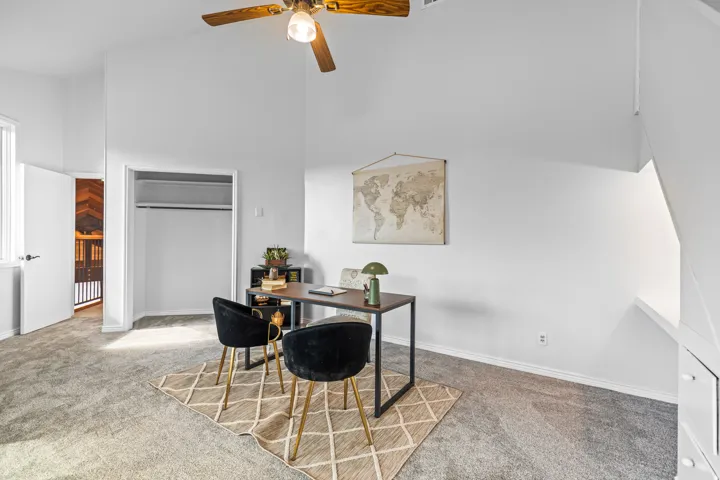 Spacious room featuring vaulted ceilings, light gray carpeting, and a ceiling fan