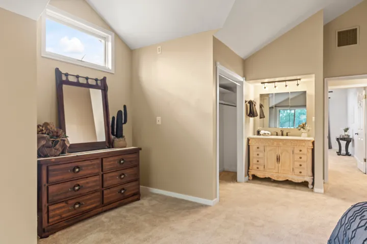 Vaulted ceiling room featuring a built-in vanity with a single sink, integrated mirror, and track lighting