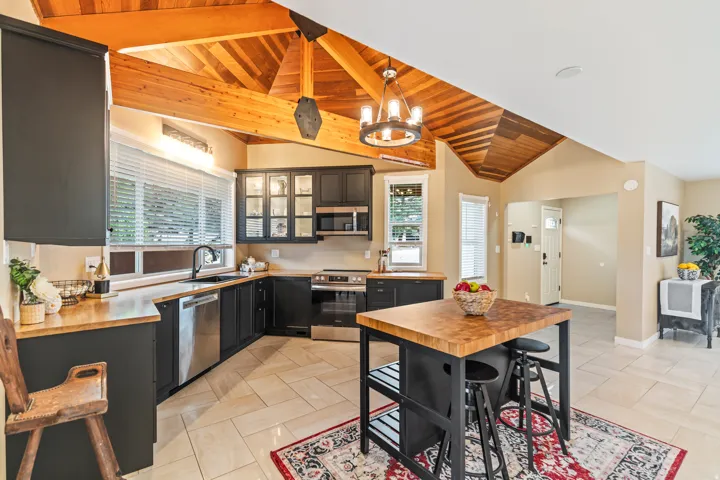 Kitchen featuring exposed wood beam vaulted ceilings, black cabinetry, stainless steel appliances, a wood butcher block island, and light tile flooring