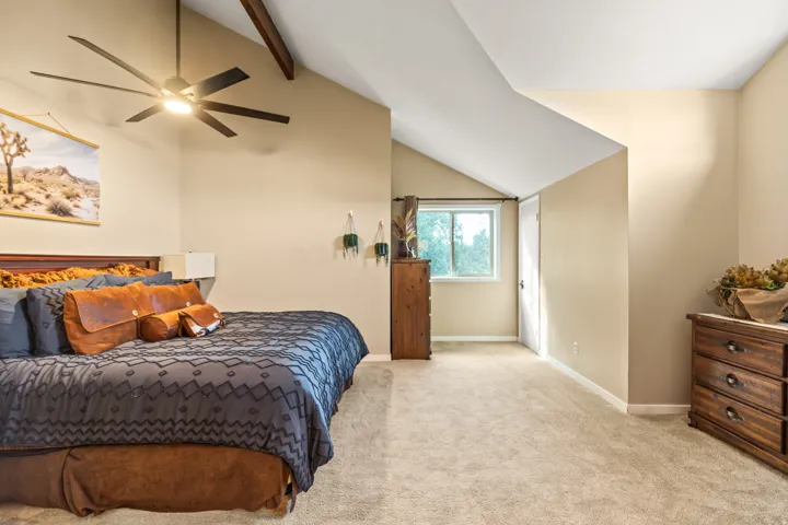 Carpeted room featuring a vaulted ceiling with exposed wood beams, a modern ceiling fan, and a window with a white trim