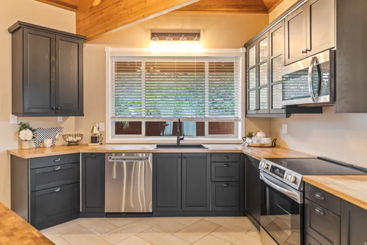Kitchen featuring dark cabinetry, wood-finish countertops, and stainless steel appliances including a built-in microwave, dishwasher, and range