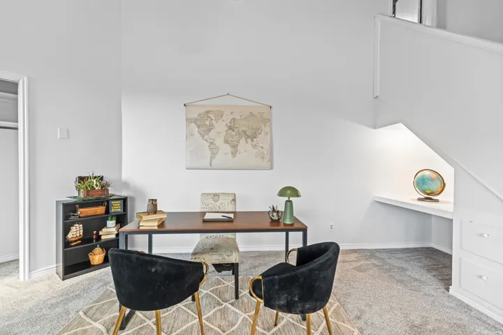Carpeted area featuring built-in shelving, white walls, and a built-in desk under the staircase