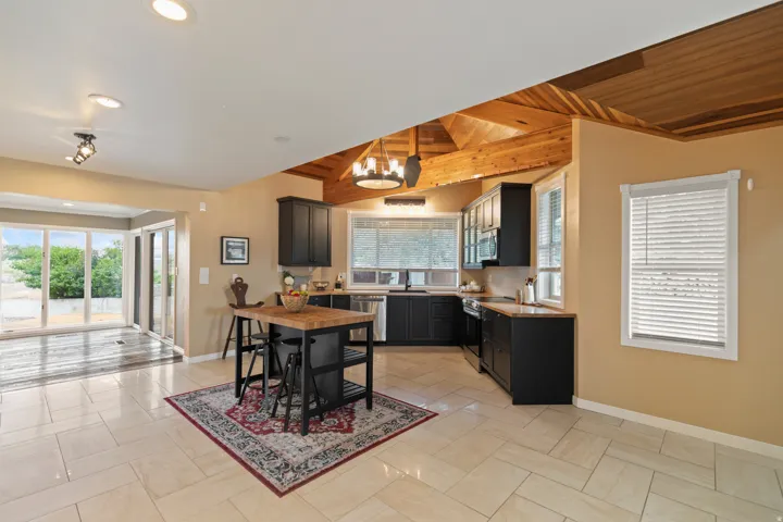 Open-concept kitchen featuring dark cabinetry, stainless steel appliances, and a wood-finish island with seating