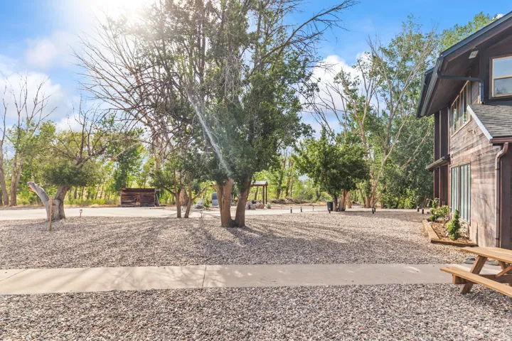 Expansive gravel driveway with a concrete walkway, bordered by mature trees and a wood-sided structure