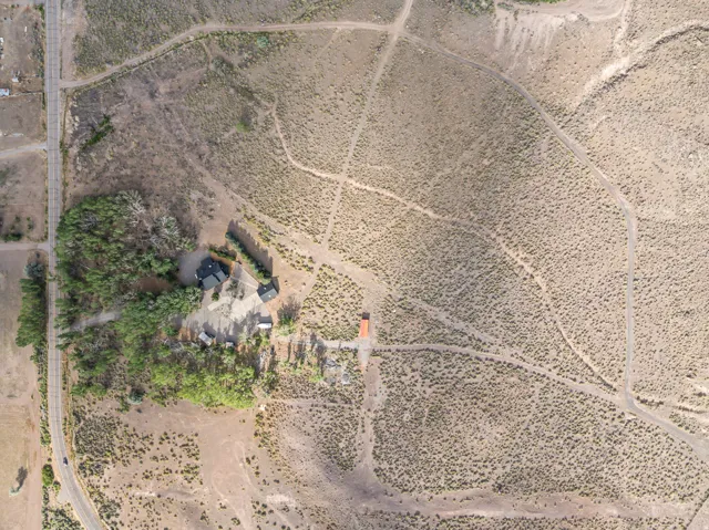Expansive aerial view showcasing a property with a dark-roofed structure and a secondary building, surrounded by arid vegetation