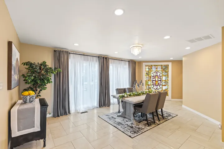 Spacious dining area featuring neutral-toned tile flooring, recessed lighting, and a decorative stained-glass window