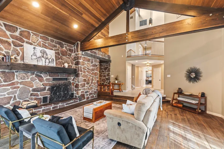 Spacious living area featuring a vaulted wood-paneled ceiling with exposed beams, a stone fireplace with a substantial wood mantel, recessed lighting, and wood-finish flooring
