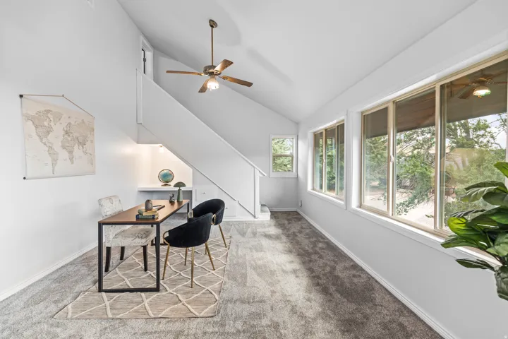 Carpeted living space with vaulted ceilings, a ceiling fan, and multiple windows